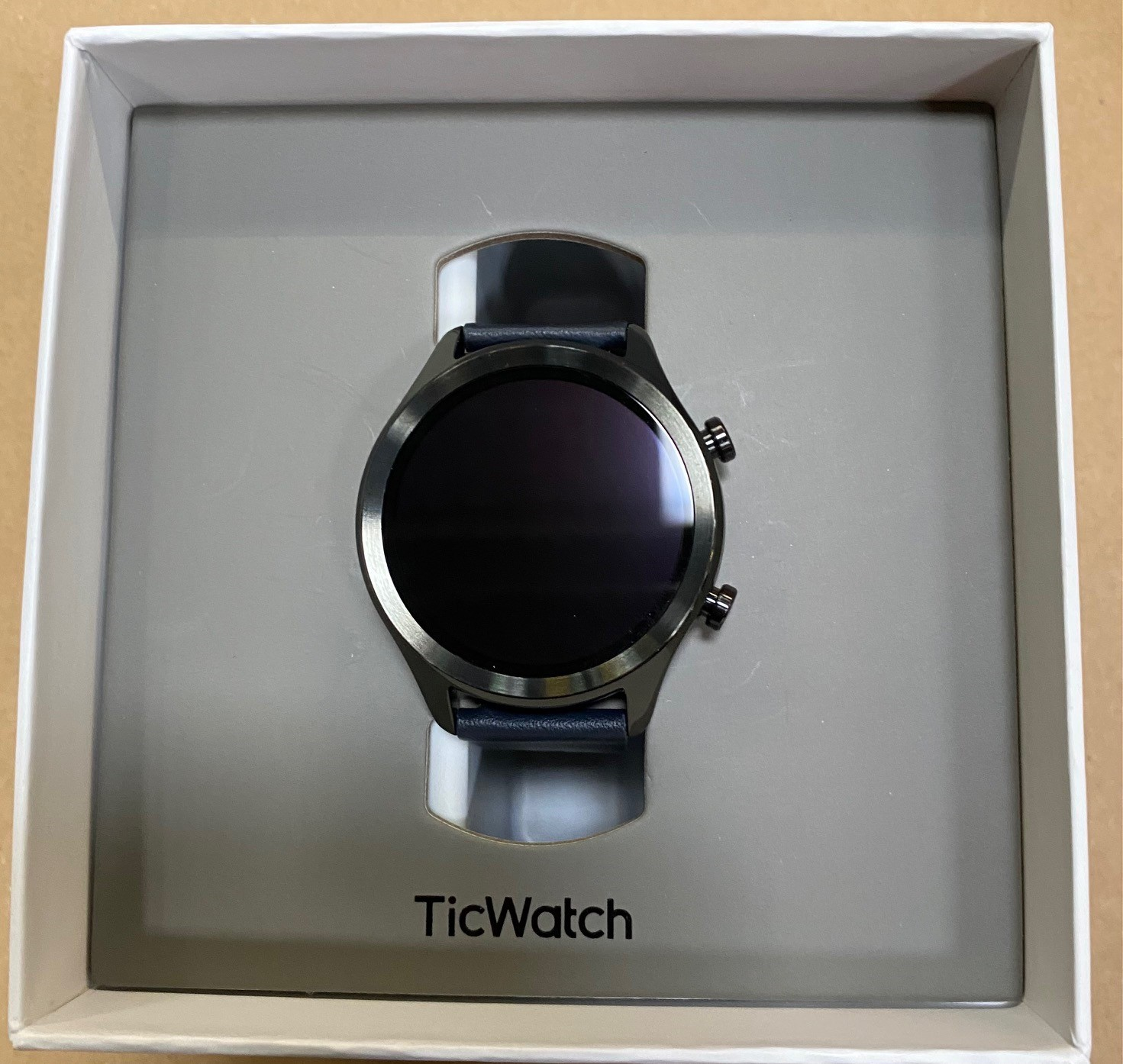 Smartwatch w otwartym pudełku, z czarnym ekranem i niebieskim paskiem.