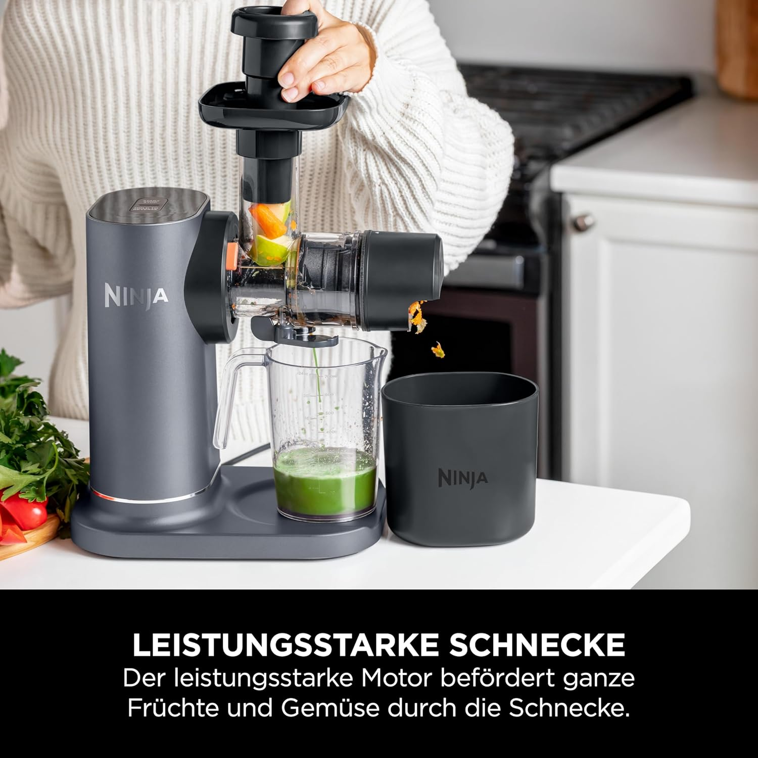 Una donna aggiunge frutta a un estrattore di succo Ninja. Un bicchiere di succo verde è sul bancone.