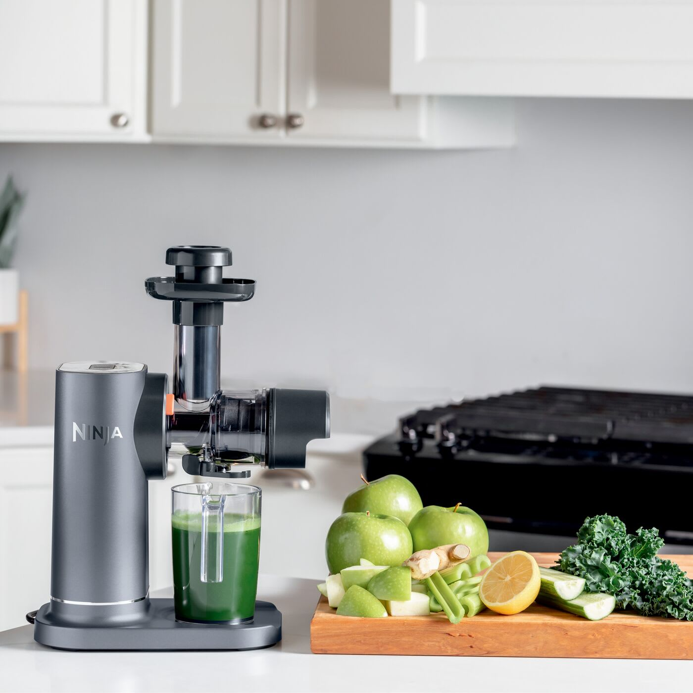 Un estrattore di succo con succo verde in un bicchiere, mele verdi, limone e verdure su una tavola.