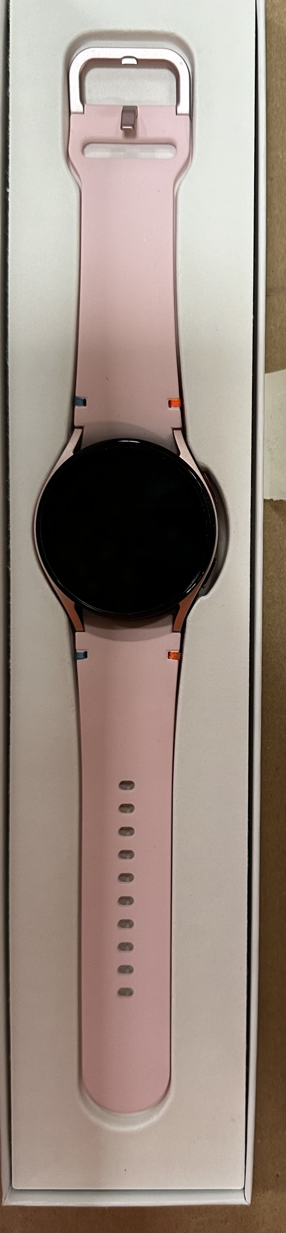 Różowy smartwatch z czarnym ekranem w otwartym pudełku.