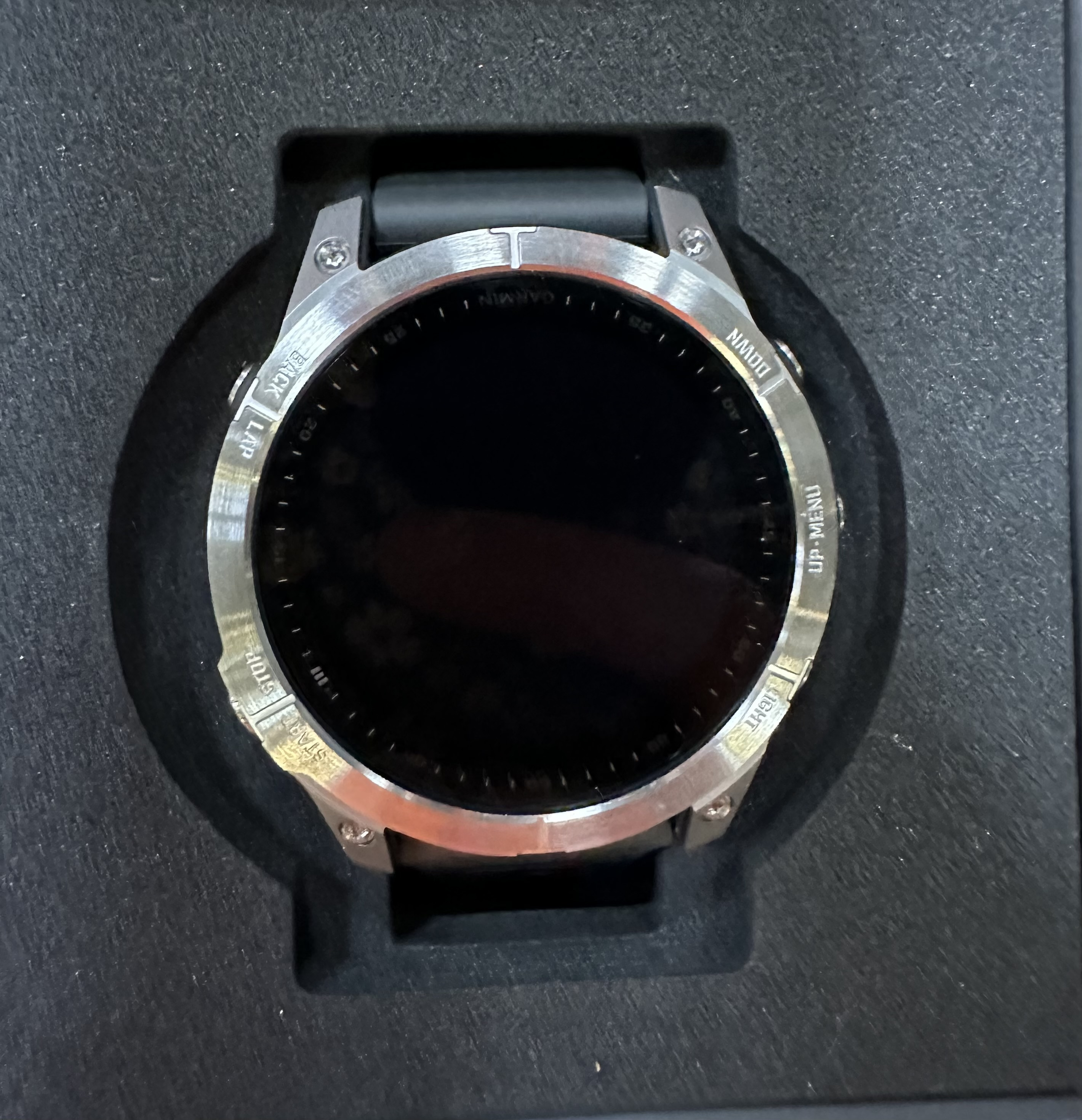 Srebrny zegarek Garmin z czarnym ekranem w czarnym pudełku.