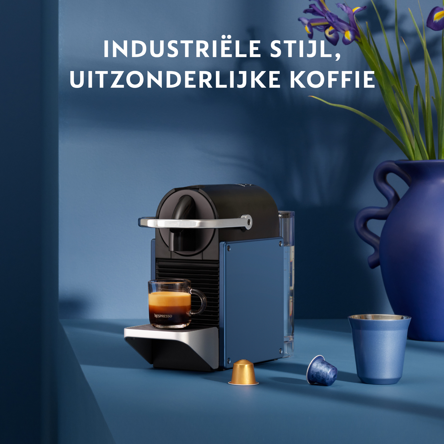 Nespresso coffee machine, blue and black, with a glass of coffee and capsules.
