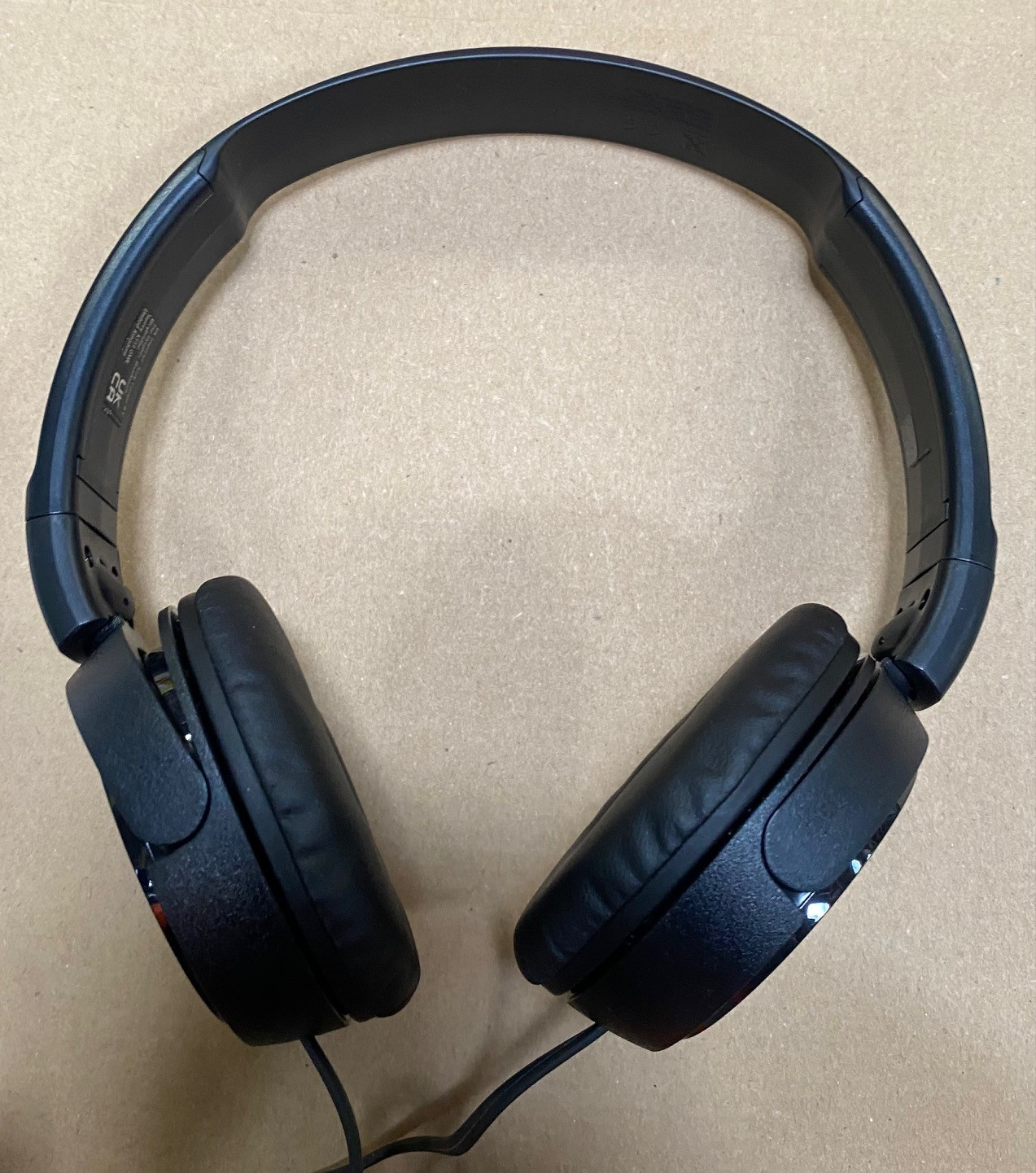 Czarne słuchawki leżące na jasnobrązowej powierzchni.