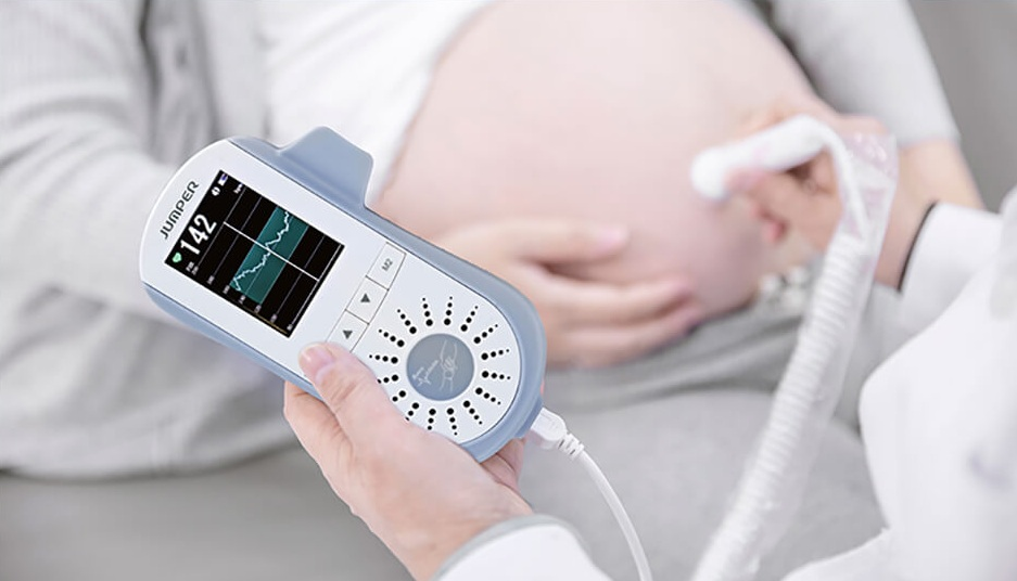 Lekarz trzyma dopplera płodowego przy brzuchu ciężarnej kobiety, w pomieszczeniu, zbliżenie.