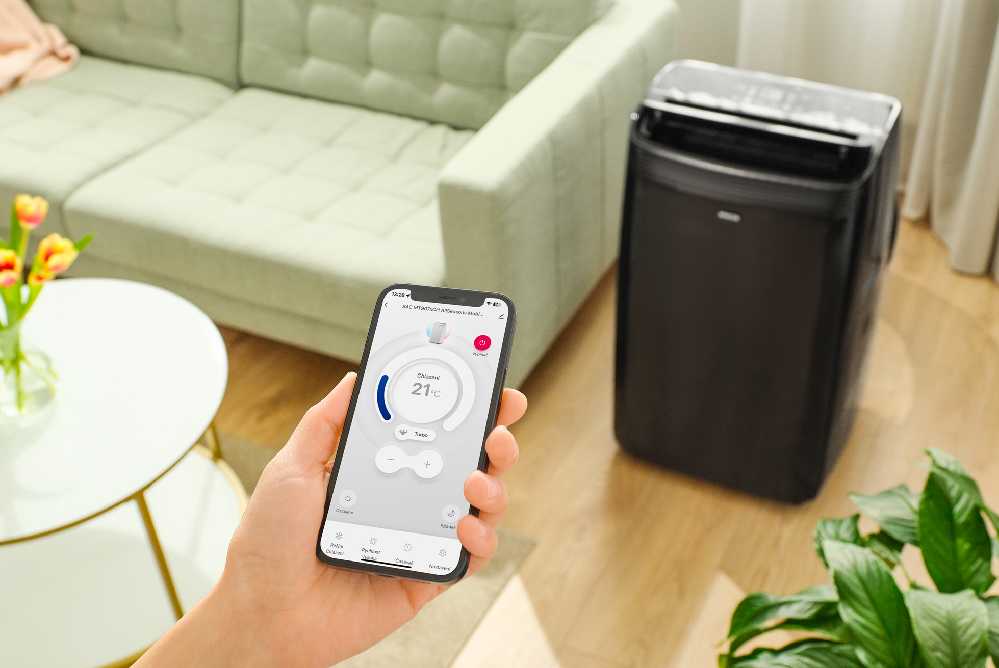 Ręka trzymająca smartfon do sterowania czarnym klimatyzatorem.