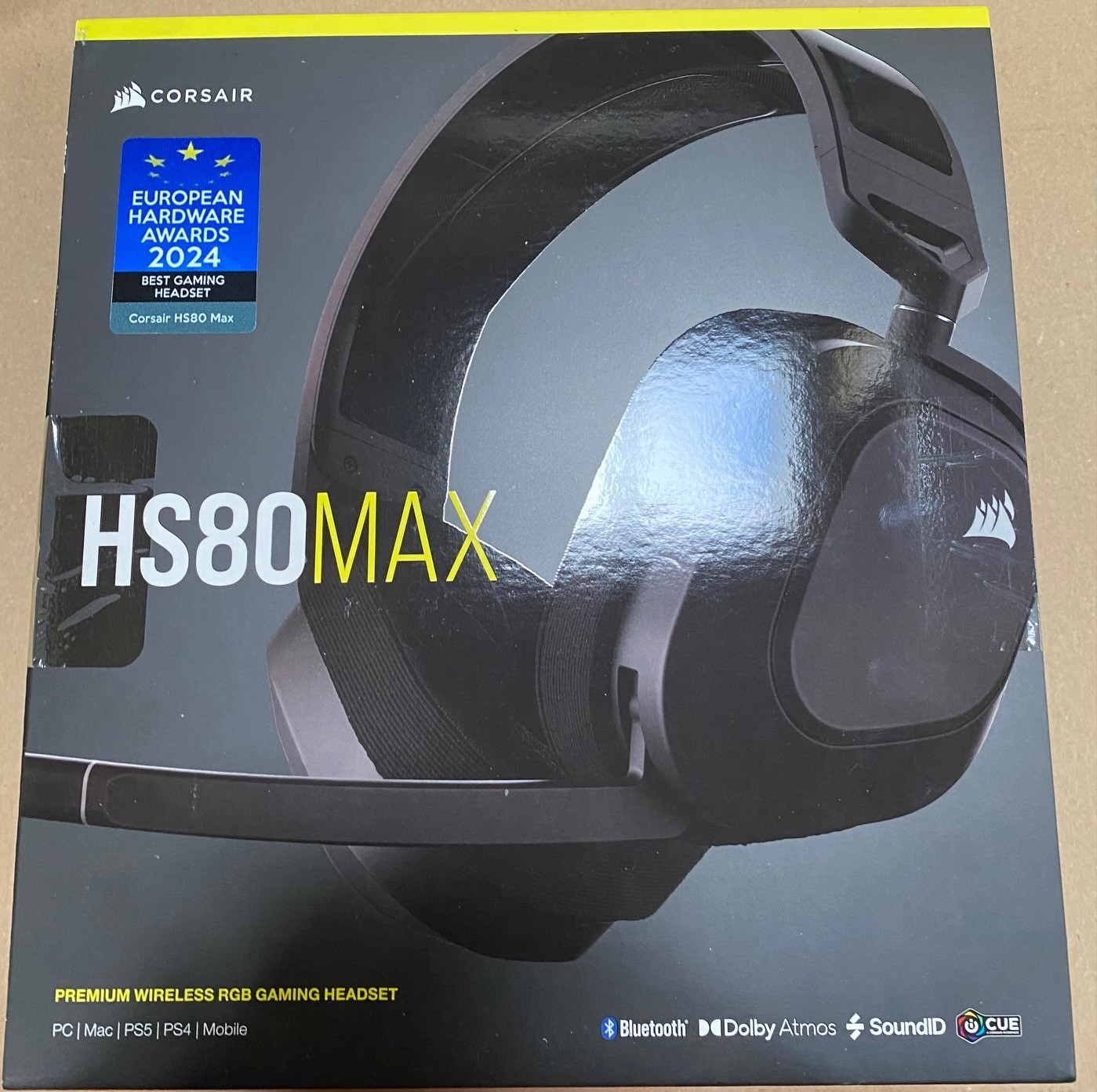 Czarne i szare pudełko słuchawek do gier Corsair HS80 MAX z naklejkami nagród. Na pudełku wyświetlana jest nazwa słuchawek.