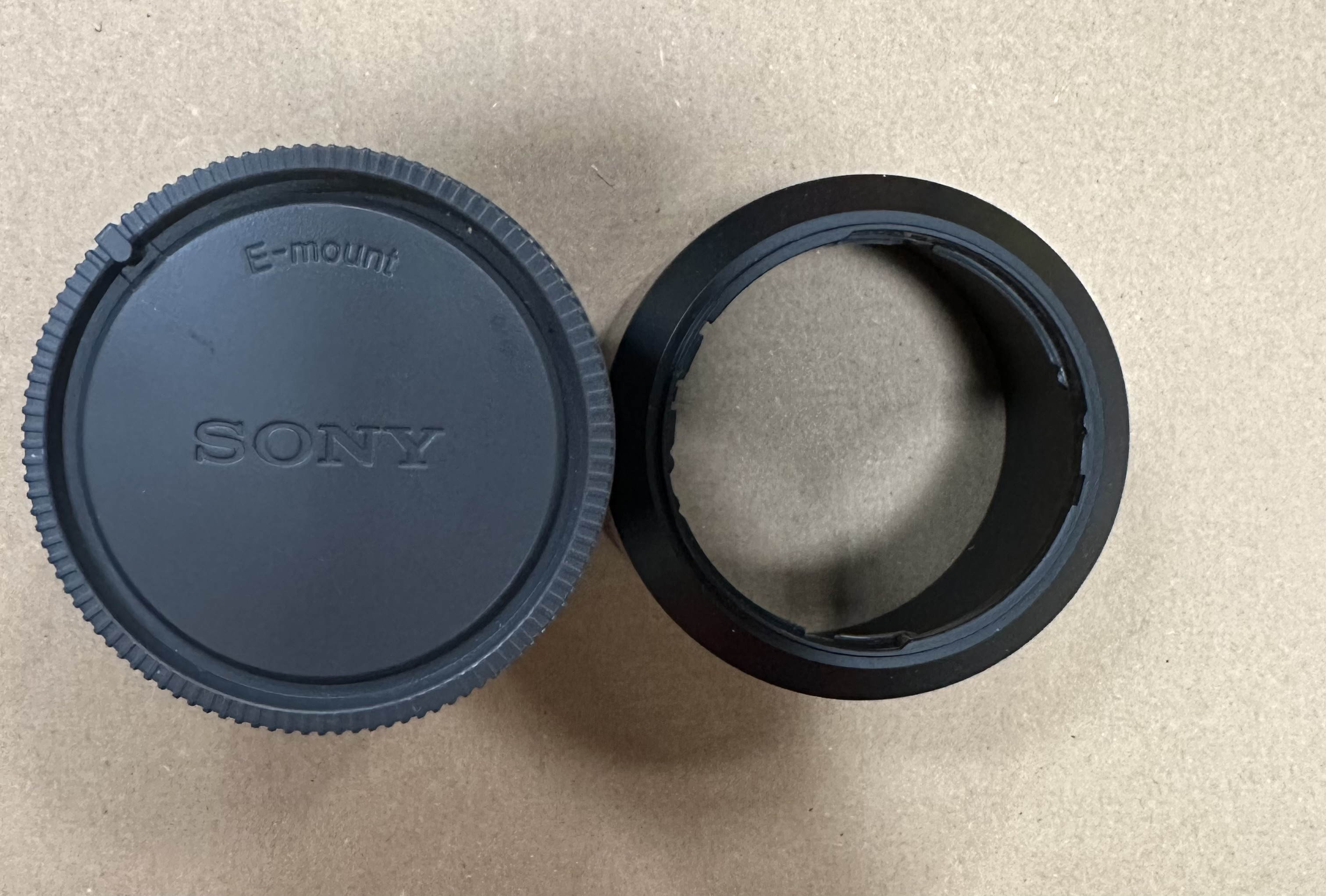 Czarna osłona obiektywu Sony i pierścień mocowania obiektywu na drewnianej powierzchni.