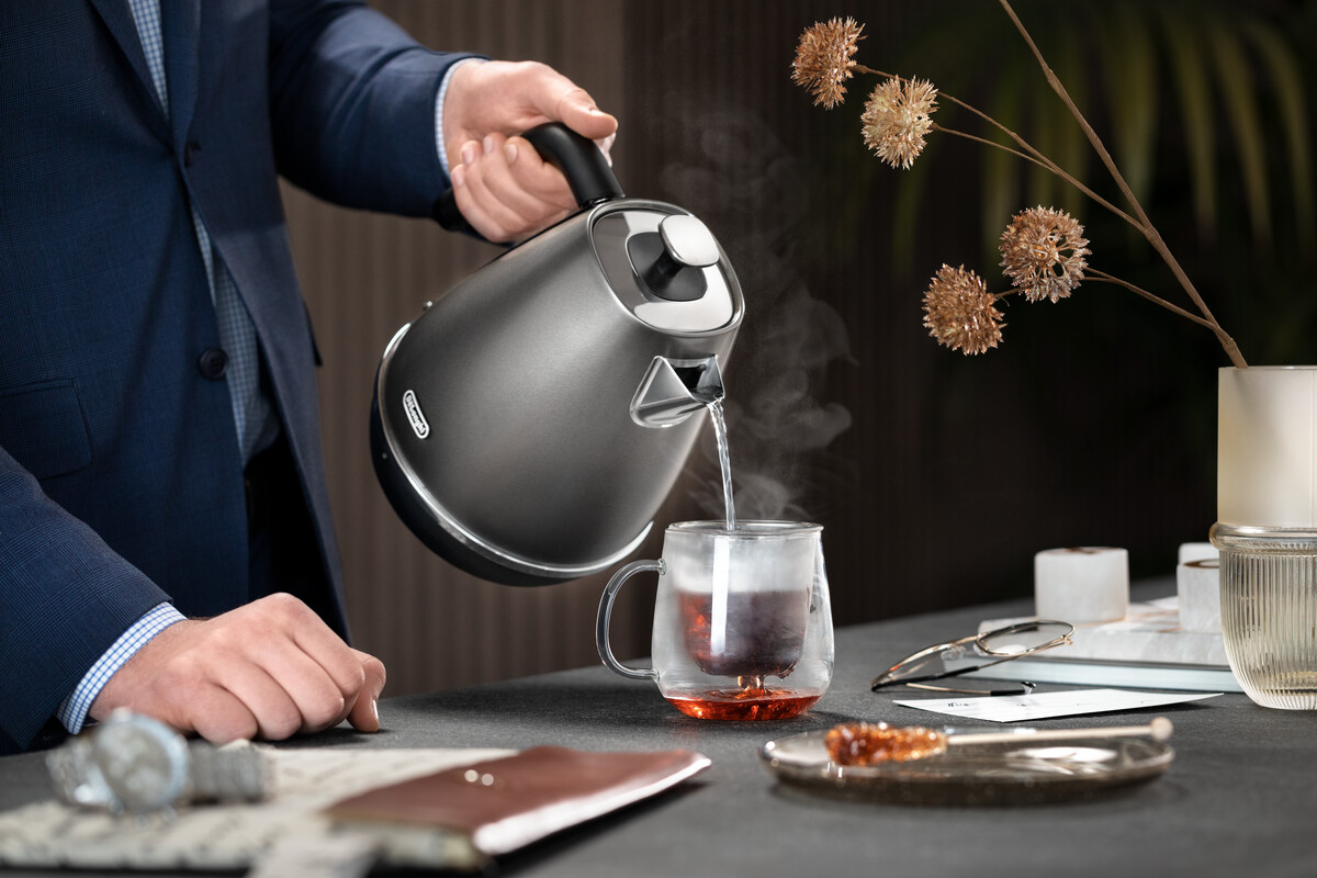 Osoba nalewająca wodę z czajnika do szklanki.