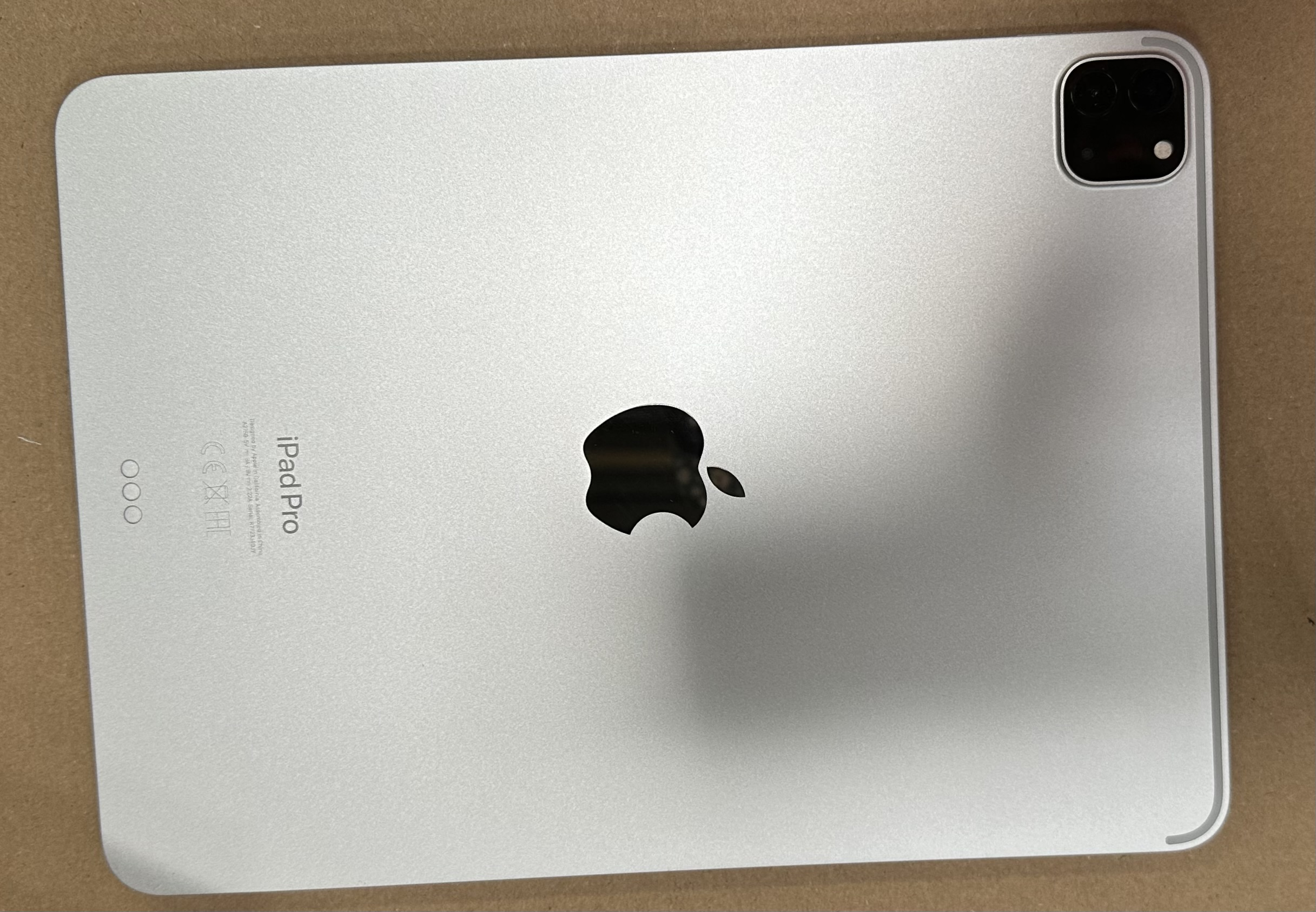 Tył srebrnego iPada Pro na brązowej powierzchni, z widocznym logo Apple i aparatem.