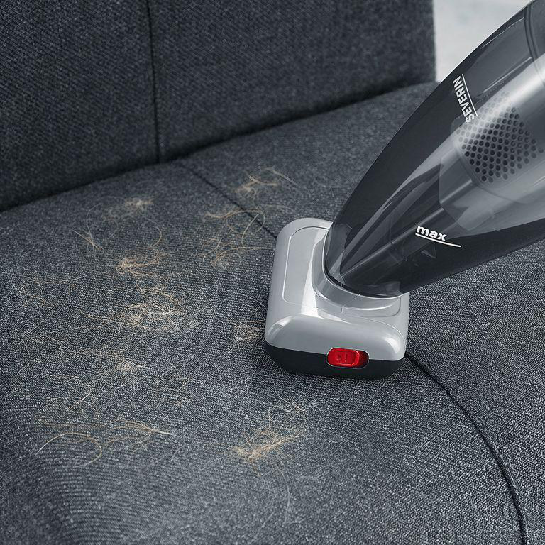 Ein Handstaubsauger auf einem grauen Sofa. Der Staubsauger saugt Tierhaare auf.