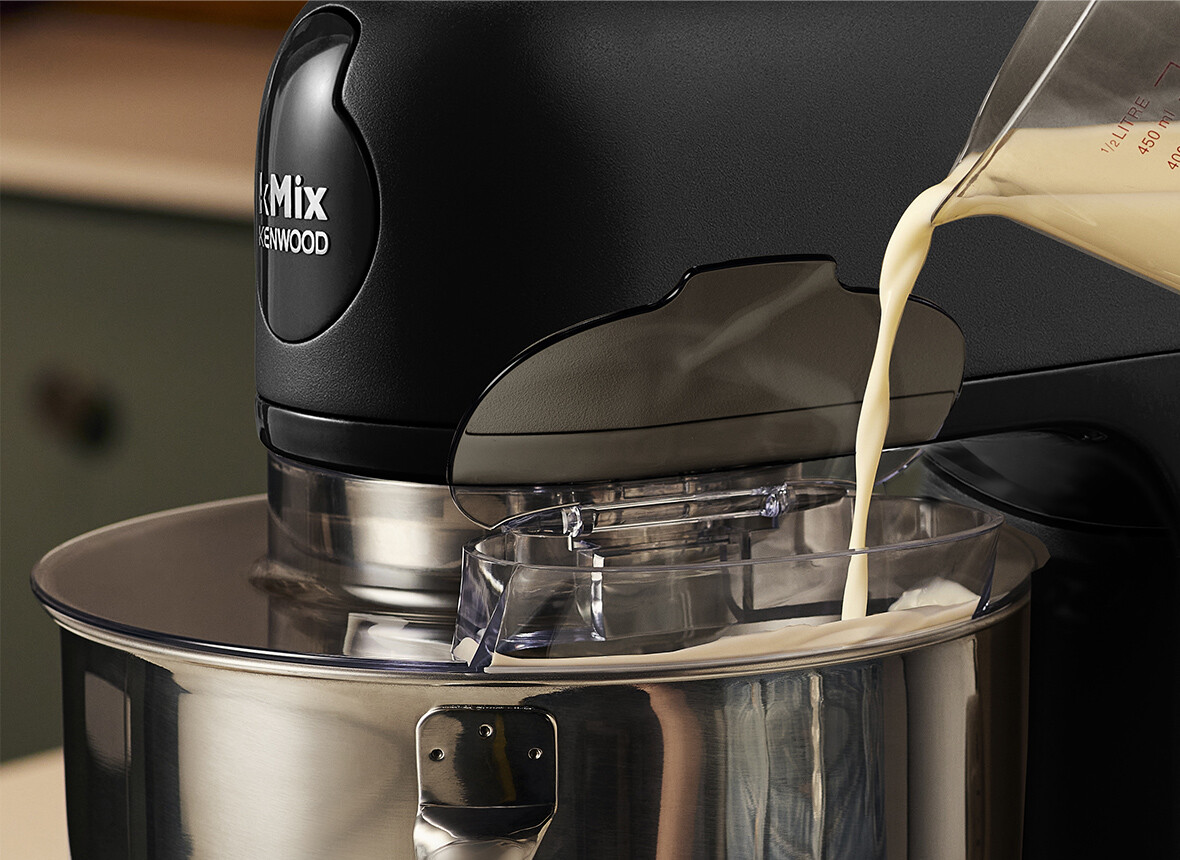 Czarny mikser kuchenny ze śmietaną wlewaną do miski. Tło jest rozmyte.