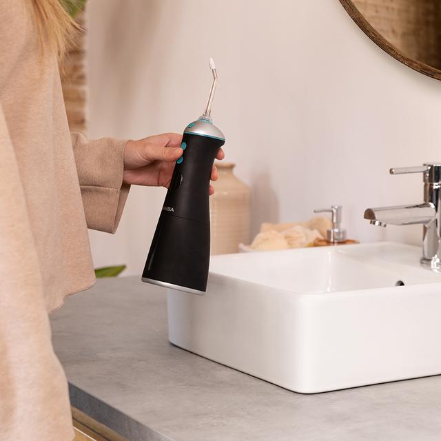 Osoba trzymająca czarny irygator nad zlewem. Scena ma miejsce w łazience z lustrem.