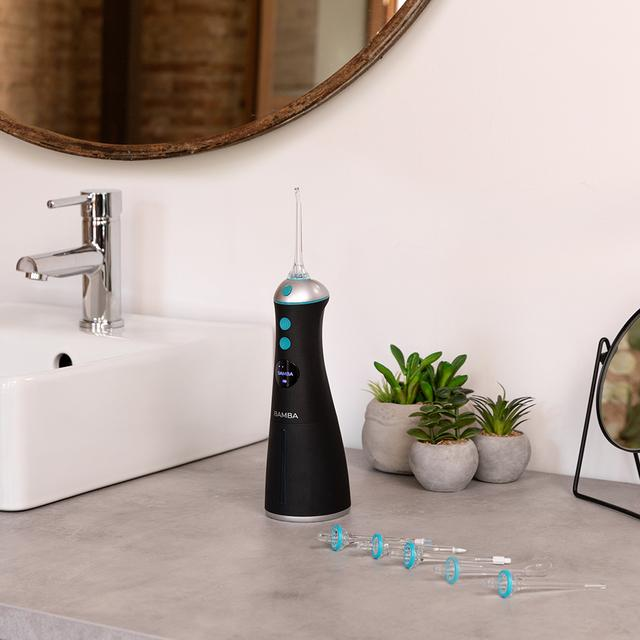 Czarny irygator do jamy ustnej na szarym blacie z umywalką, lustrem i roślinami w tle.