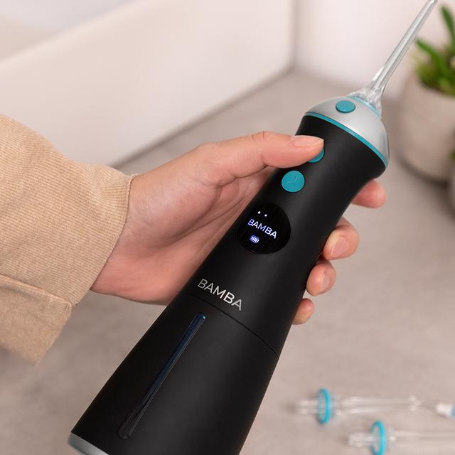 Czarny i niebieski irygator do jamy ustnej trzymany w dłoniach osoby. Urządzenie posiada przyciski i wyświetlacz cyfrowy.