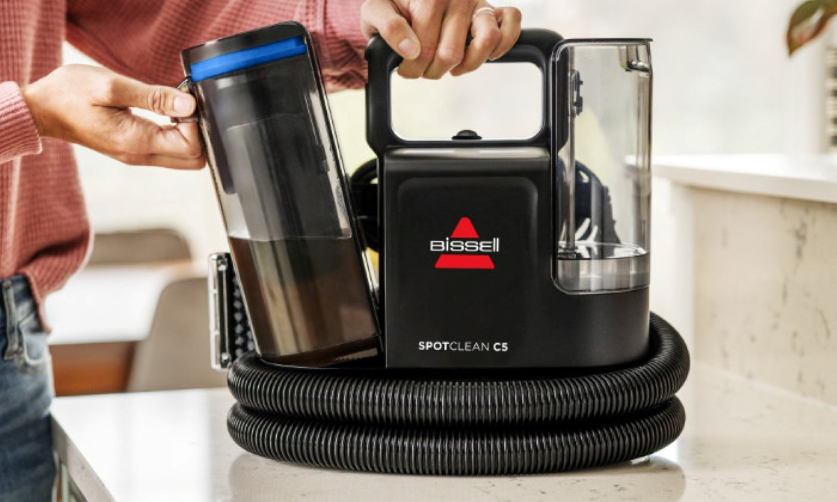 Osoba trzyma czarny i szary odkurzacz Bissell SpotClean C5.