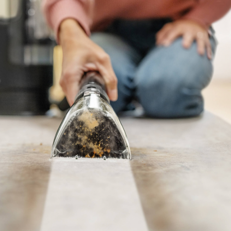 Osoba czyszcząca jasną podłogę głowicą odkurzacza.