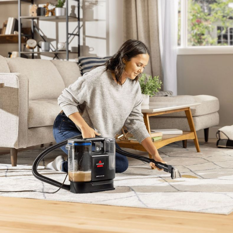Kobieta klęczy i używa odkurzacza do dywanów Bissell, czyszcząc biały dywan.