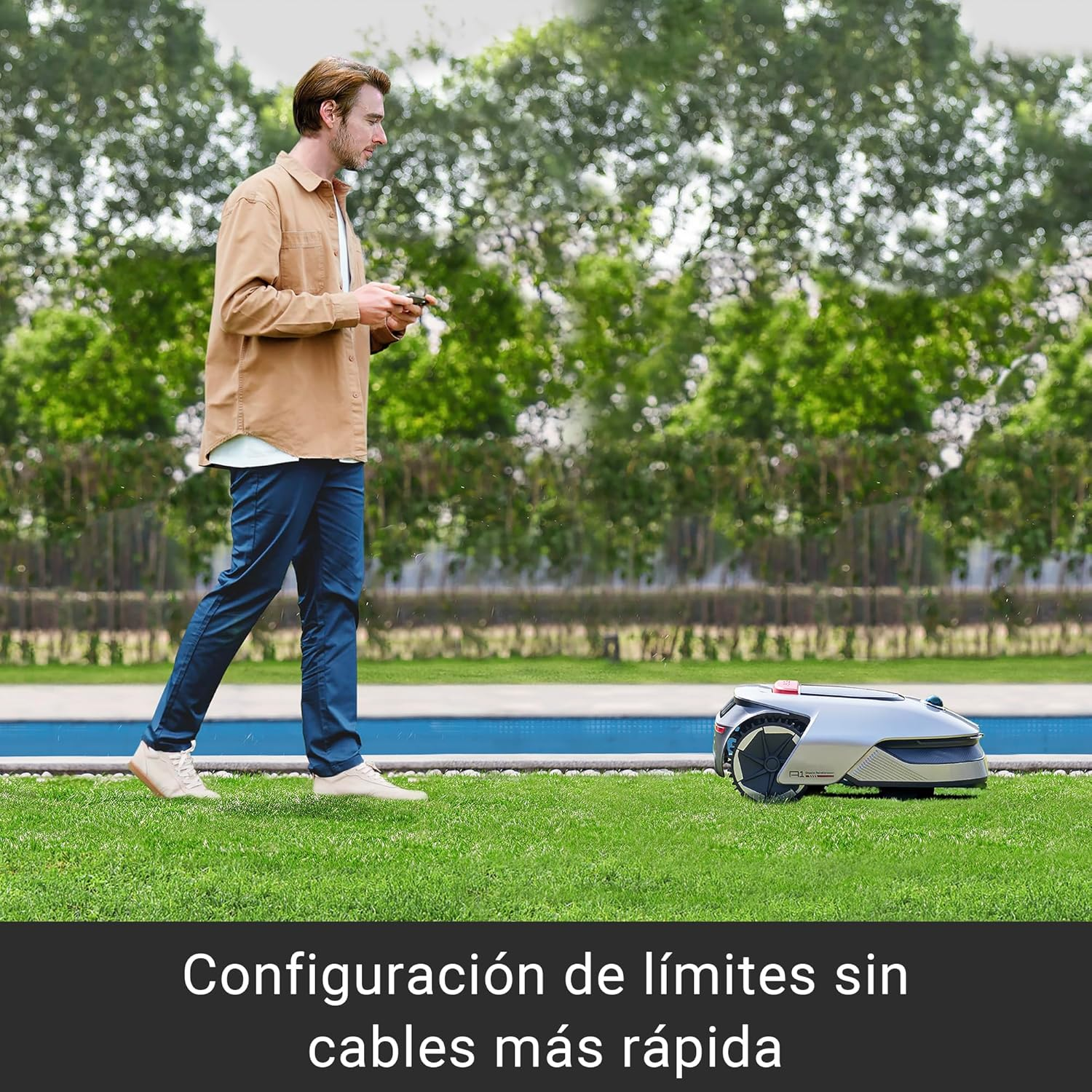 Hombre configurando un cortacésped robótico en césped. Árboles y una piscina en el fondo.