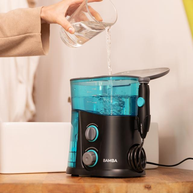 Osoba nalewa wodę do niebiesko-czarnego irygatora Bamba. Beżowy stół, biały zlew w tle.