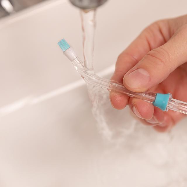 Ręka trzymająca końcówkę irygatora dentystycznego pod bieżącą wodą, pokazująca proces czyszczenia.