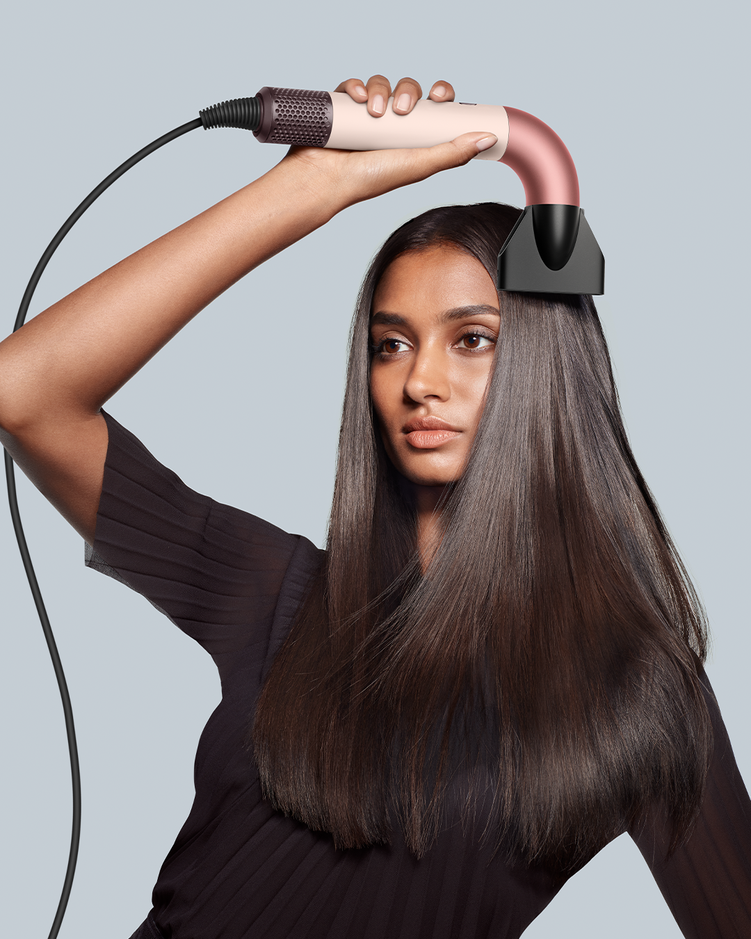 Una mujer sosteniendo un secador de pelo sobre su cabeza, enfocándose en su cabello y la boquilla.