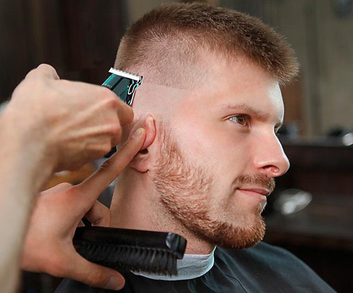 Fryzjer używa elektrycznej maszynki do strzyżenia włosów mężczyzny, zbliżenie.