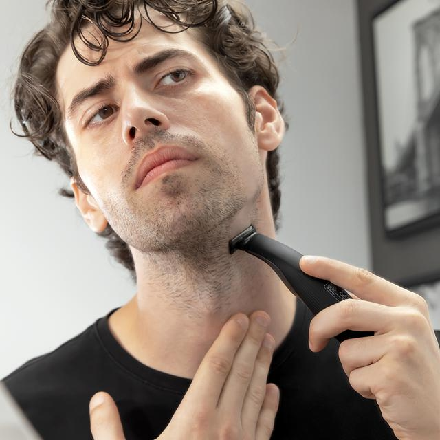 Mężczyzna goli brodę trymerem. Zbliżenie, patrząc w dół, czarny t-shirt.