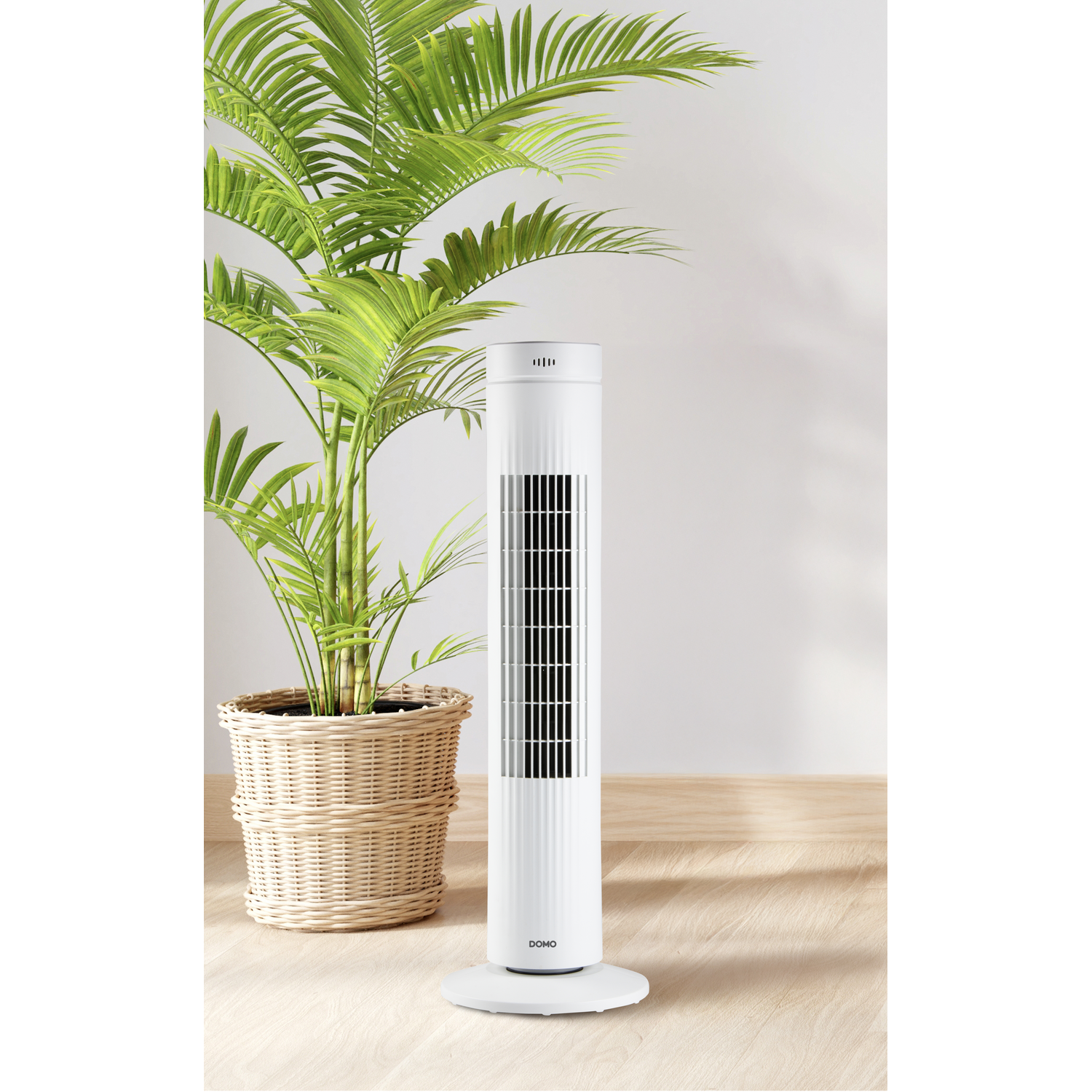 Witte torenventilator naast een groene plant in pot, houten vloer.