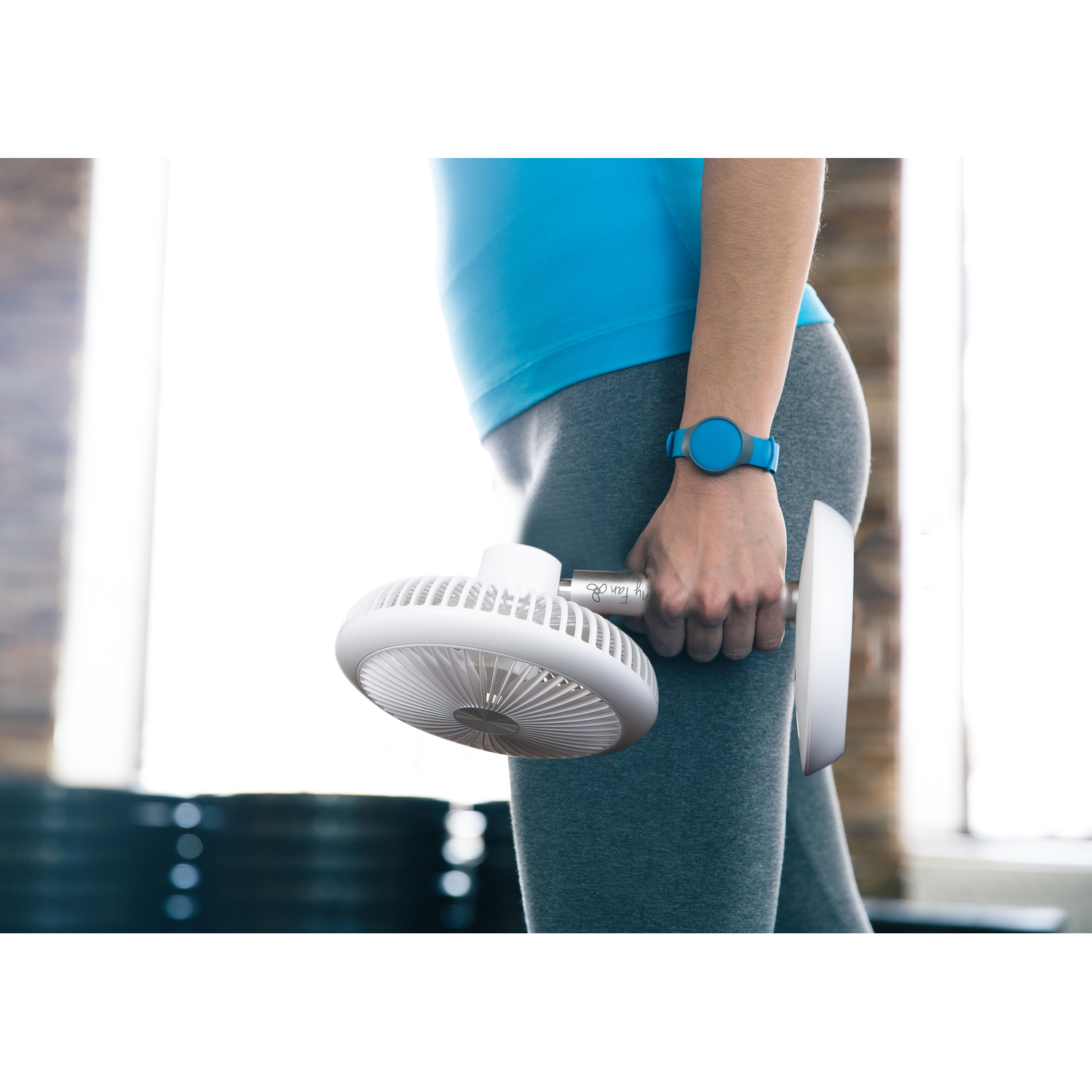 A person holding a white fan. They wear a blue watch and grey workout clothes.