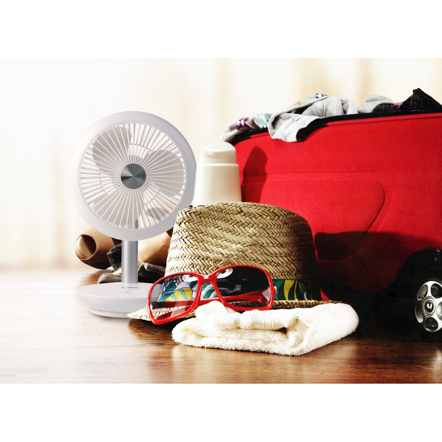 Fan, sunglasses, hat, towel, and luggage on a table.
