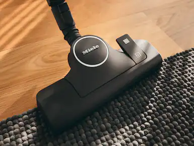 Gri bir halı üzerinde bir elektrikli süpürge başlığı. Elektrikli süpürge başlığı, beyaz logolu siyahtır.