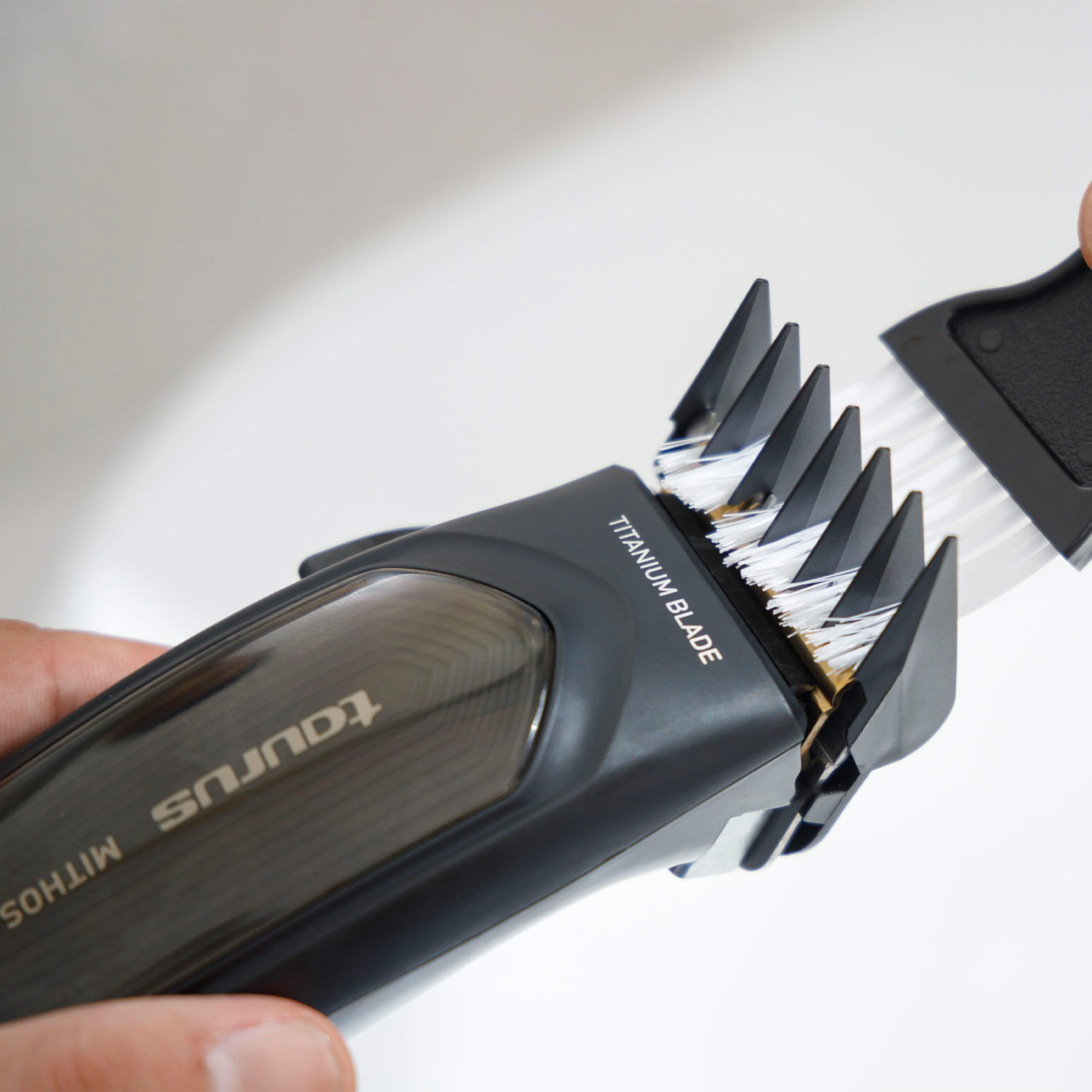 Una cortadora de pelo negra con un cepillo limpiando las cuchillas. El texto en la cortadora dice 'Titanium Blade'.