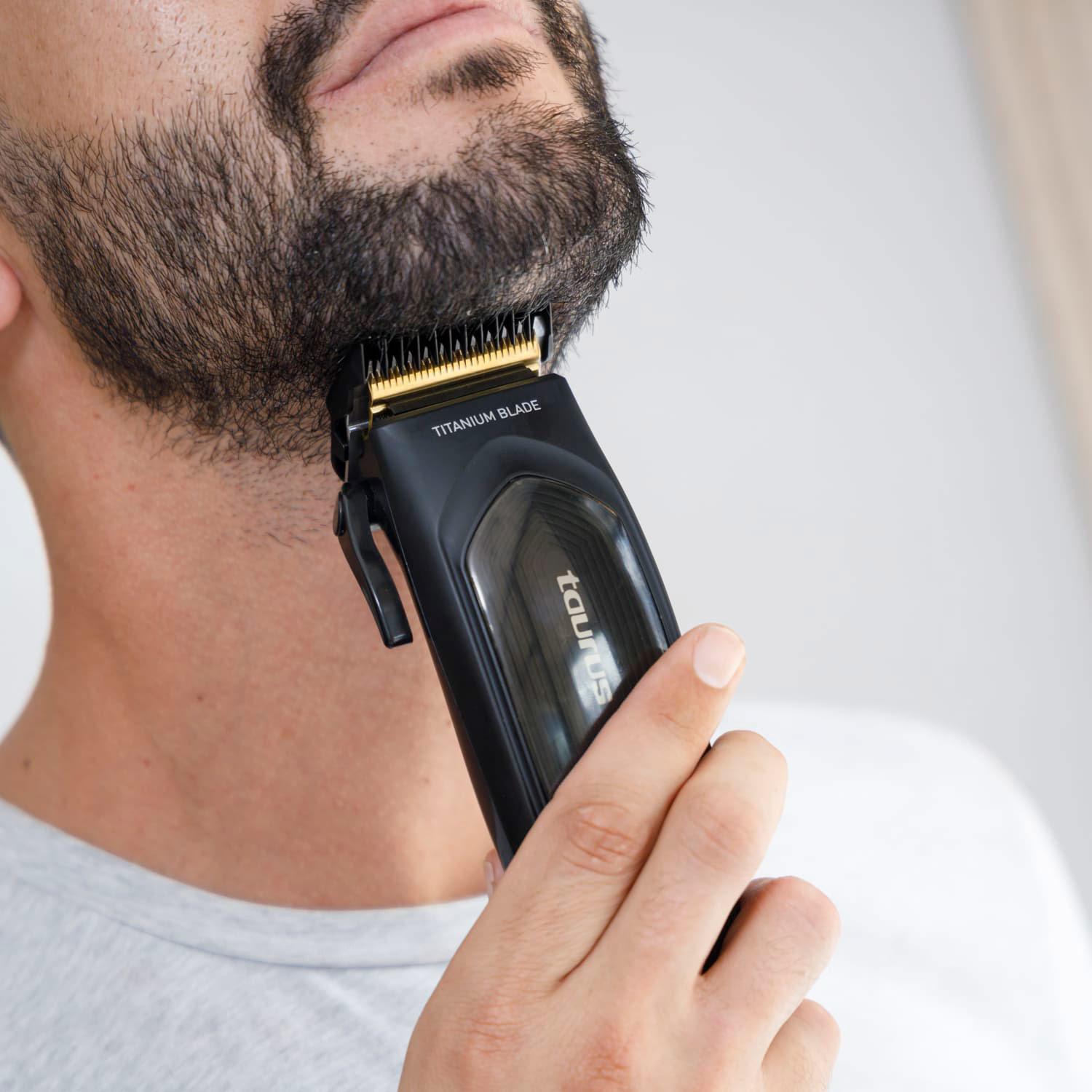 Hombre afeitándose la barba con recortadora negra y dorada. Cuchilla de titanio, marca Taurus.