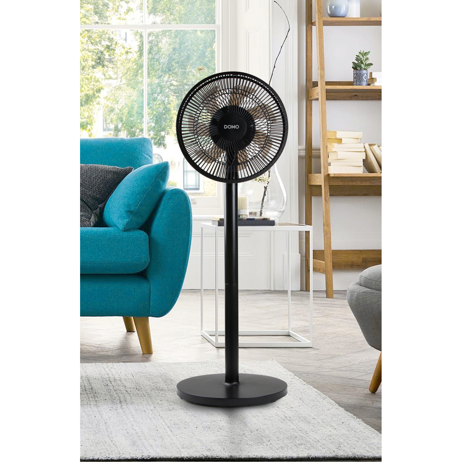 Un ventilateur sur pied noir dans une pièce avec un canapé bleu et une fenêtre, une table blanche et un tapis.