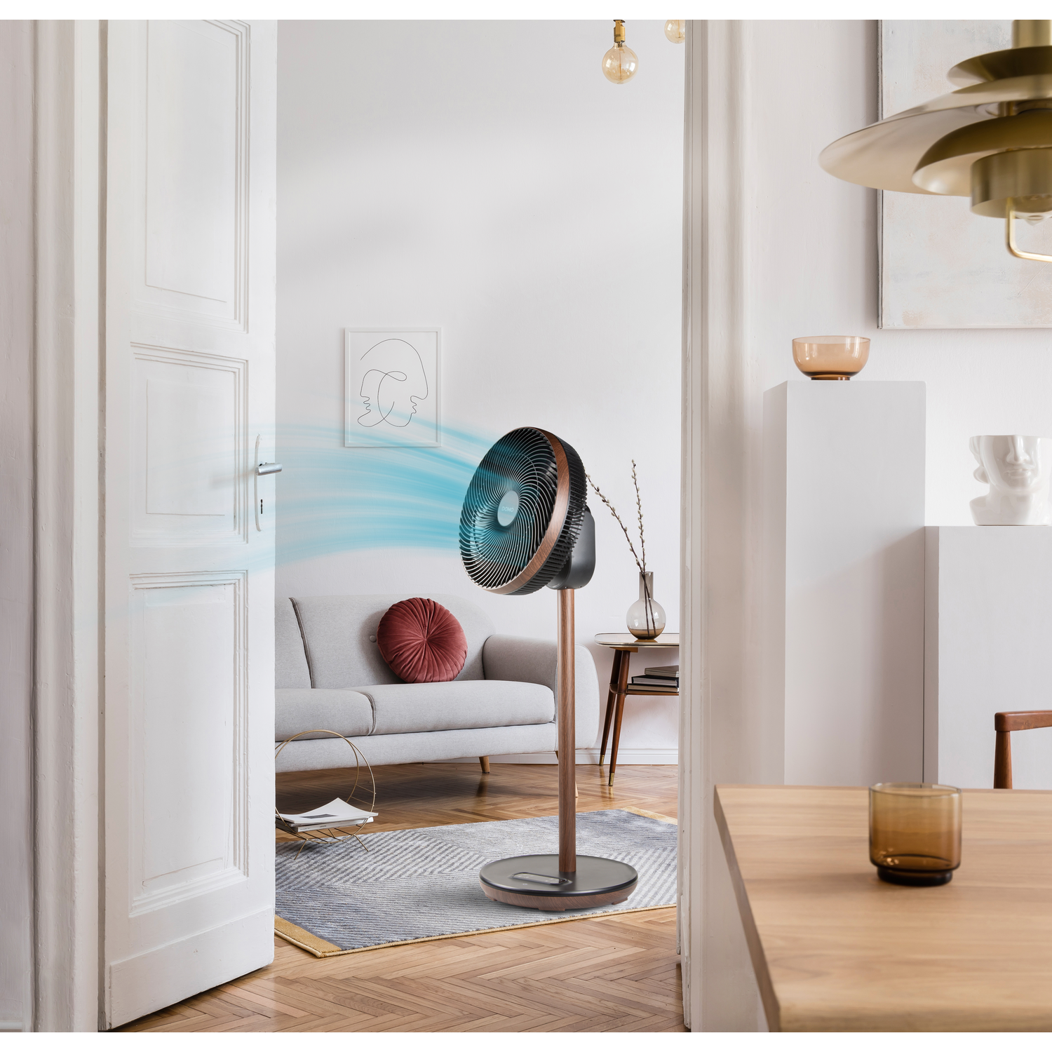 Un ventilateur moderne sur pied, soufflant de l'air dans une pièce avec des meubles et de la décoration.