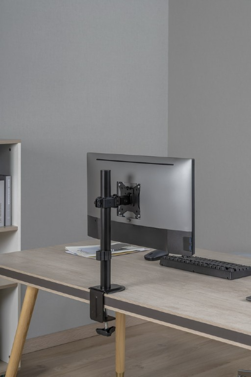 Monitor egy állványon az asztalon, asztal és fal a háttérben.