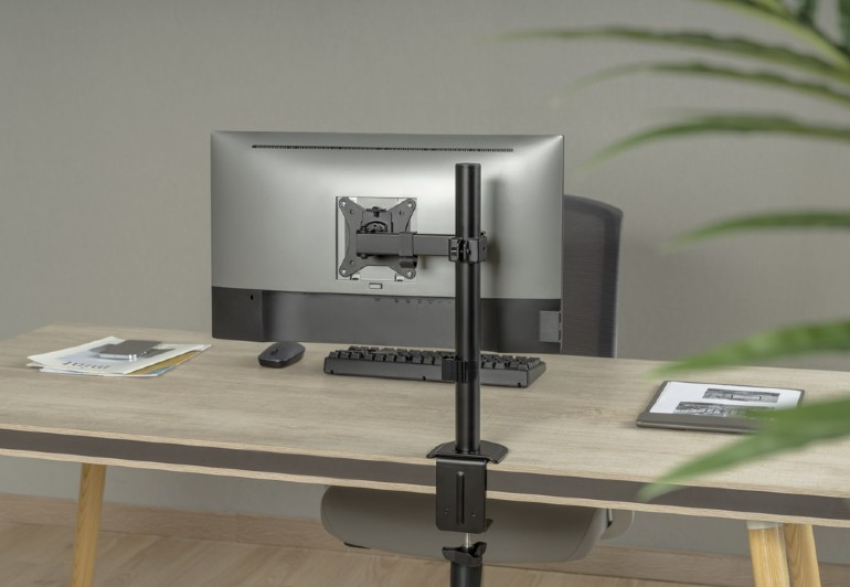 Egy fekete monitortartó, ami egy monitort tart. A monitor egy fa asztalon van, billentyűzettel.