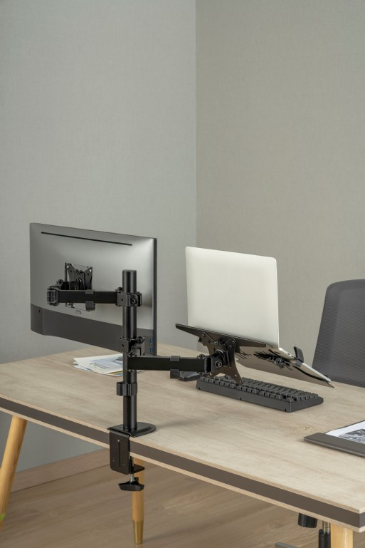 Monitor és laptop az asztalon. Fekete monitor tartó balra. A laptop jobbra.