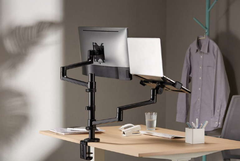 Egy asztal monitorral és laptopállvánnyal. A tárgyak egy világosbarna asztalon vannak.