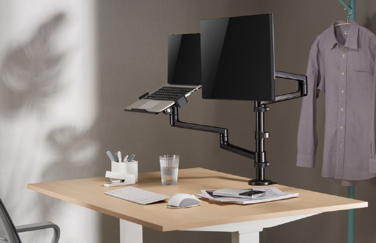 Asztal laptop- és monitorkarral. Laptop állványon, monitor jobbra, kiegészítők az asztalon.