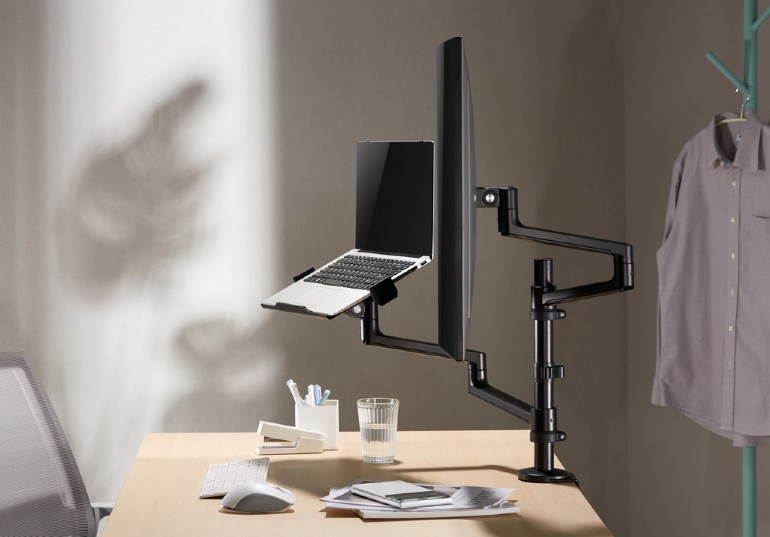 Irodai beállítás laptop, monitor és kiegészítőkkel. Asztal és fal látható.