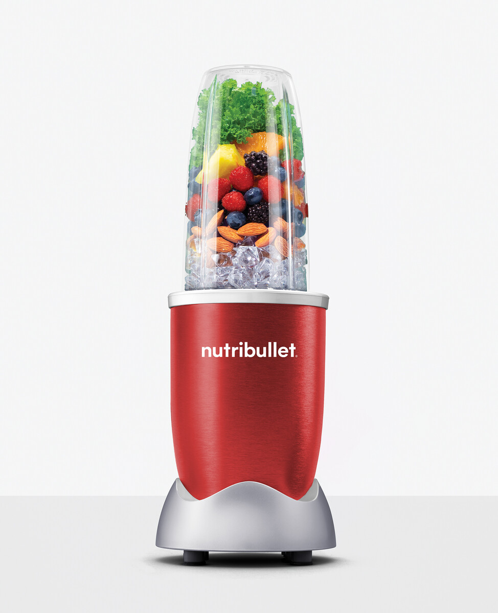Czerwony blender Nutribullet z owocami i lodem w środku. Jest na białym tle.