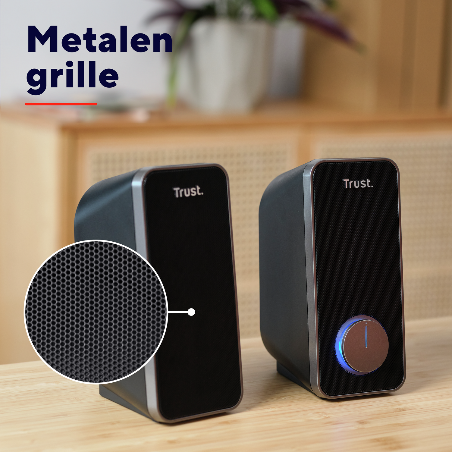 Two black speakers. One has a close-up of the speaker grill. Wooden table background.