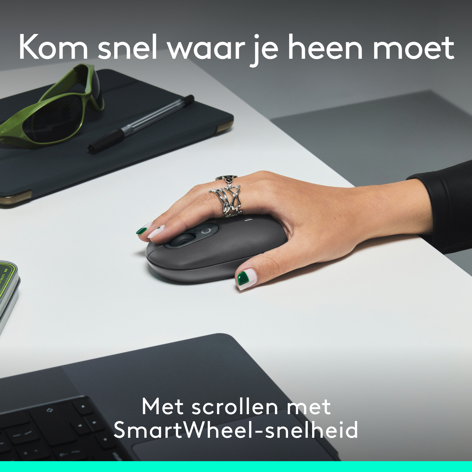 Een hand die een donkergrijze muis gebruikt op een wit oppervlak. Groene bril en pen ook aanwezig.