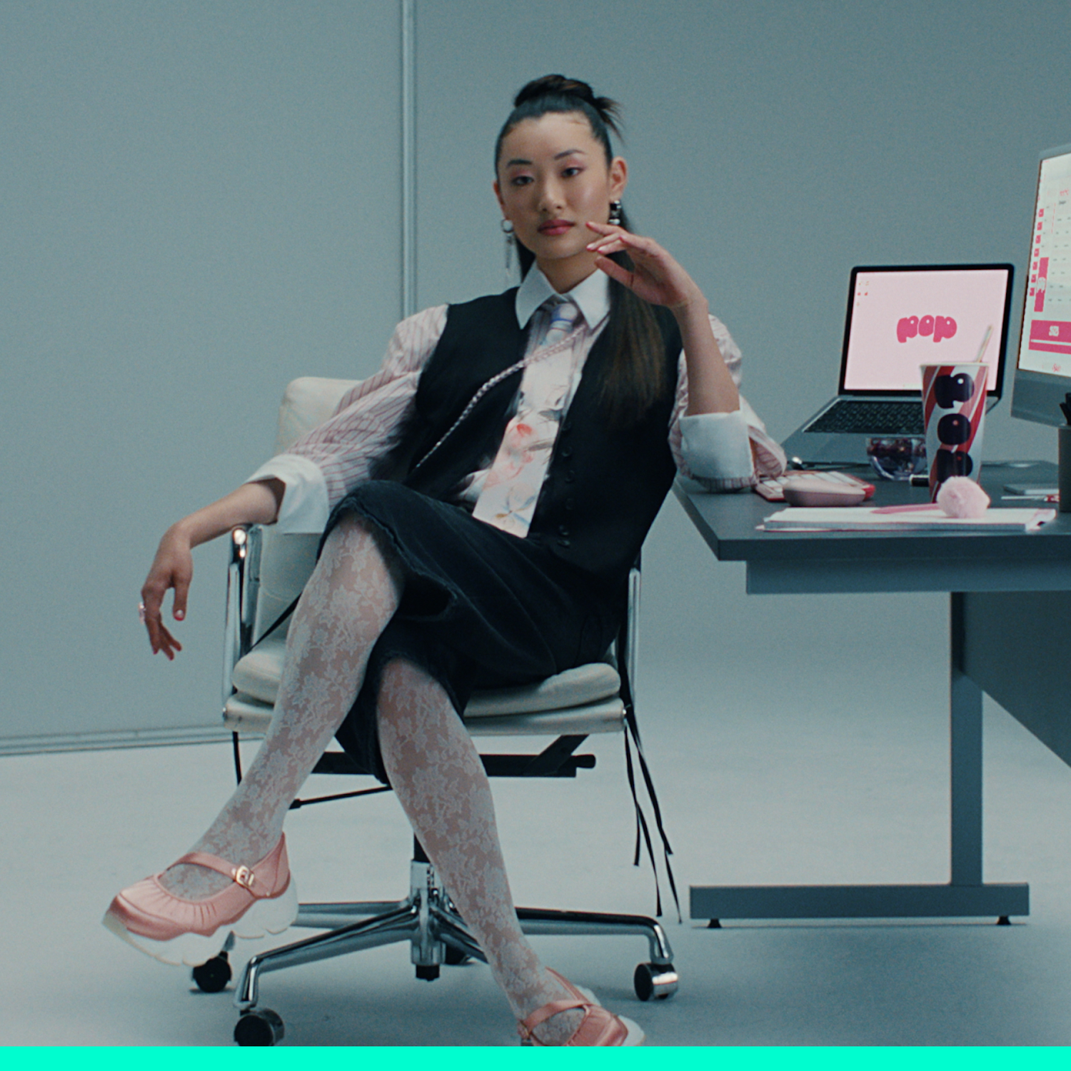 Een vrouw in zakelijke kleding zit aan een bureau met een laptop en een monitor.