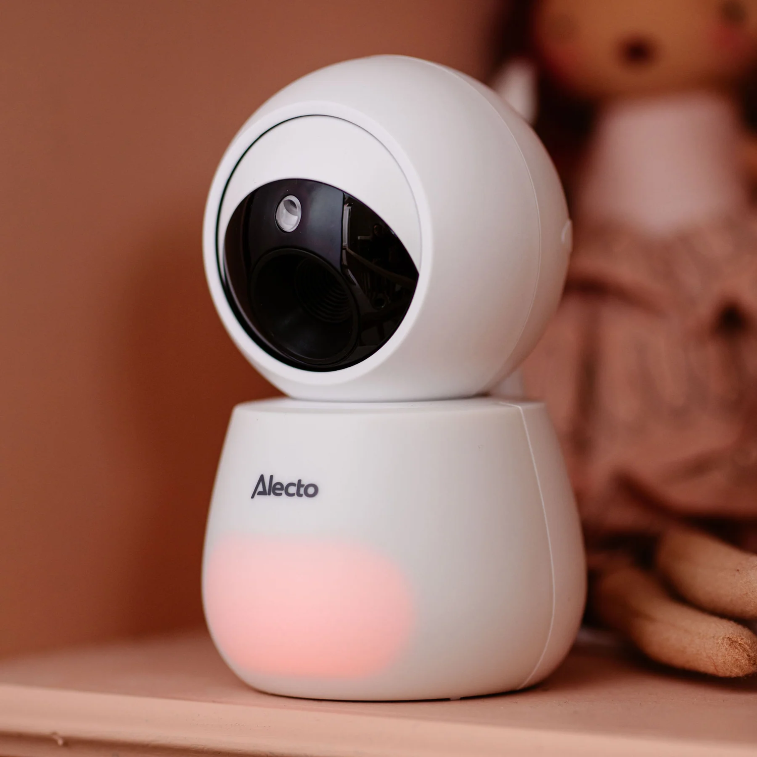 White baby monitor with a pink light on a shelf.