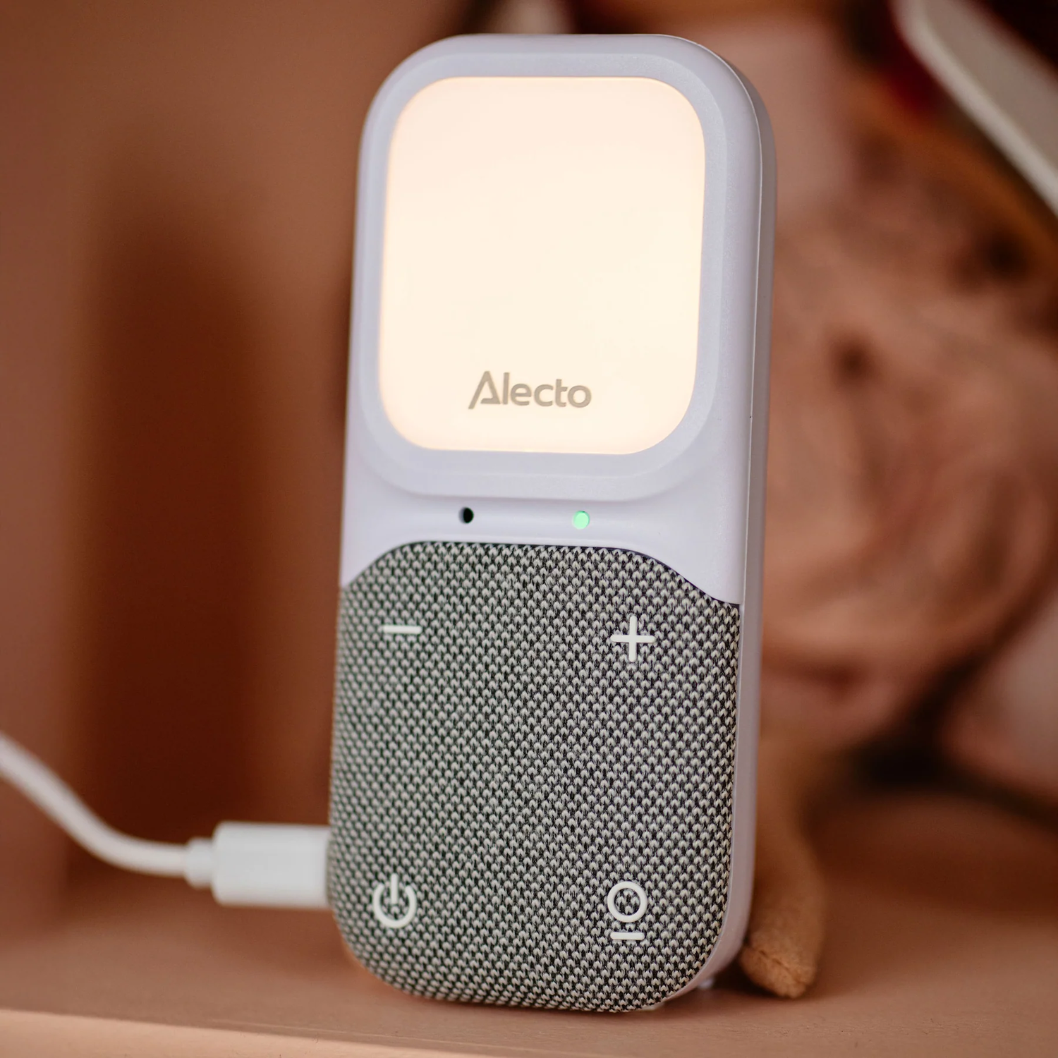 A white baby monitor with a light up screen. It is charging with a white USB cable.