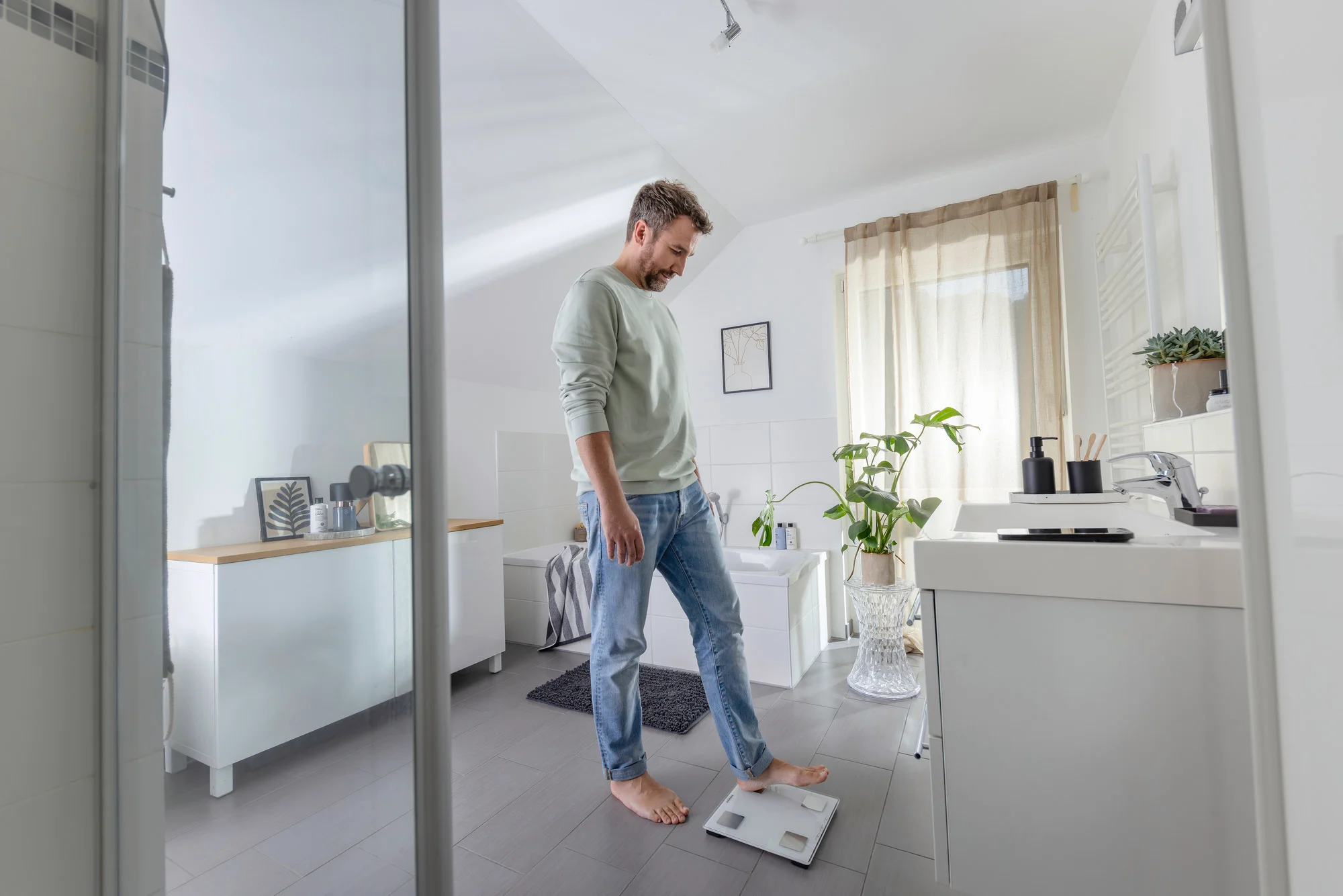 Un homme debout sur une balance dans une salle de bain lumineuse.