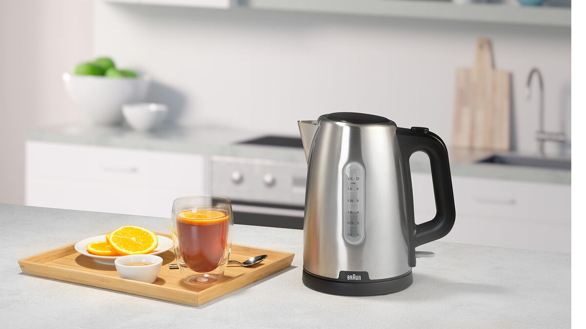 Czajnik, szklanka herbaty z plasterkiem pomarańczy i drewniana taca na blacie.