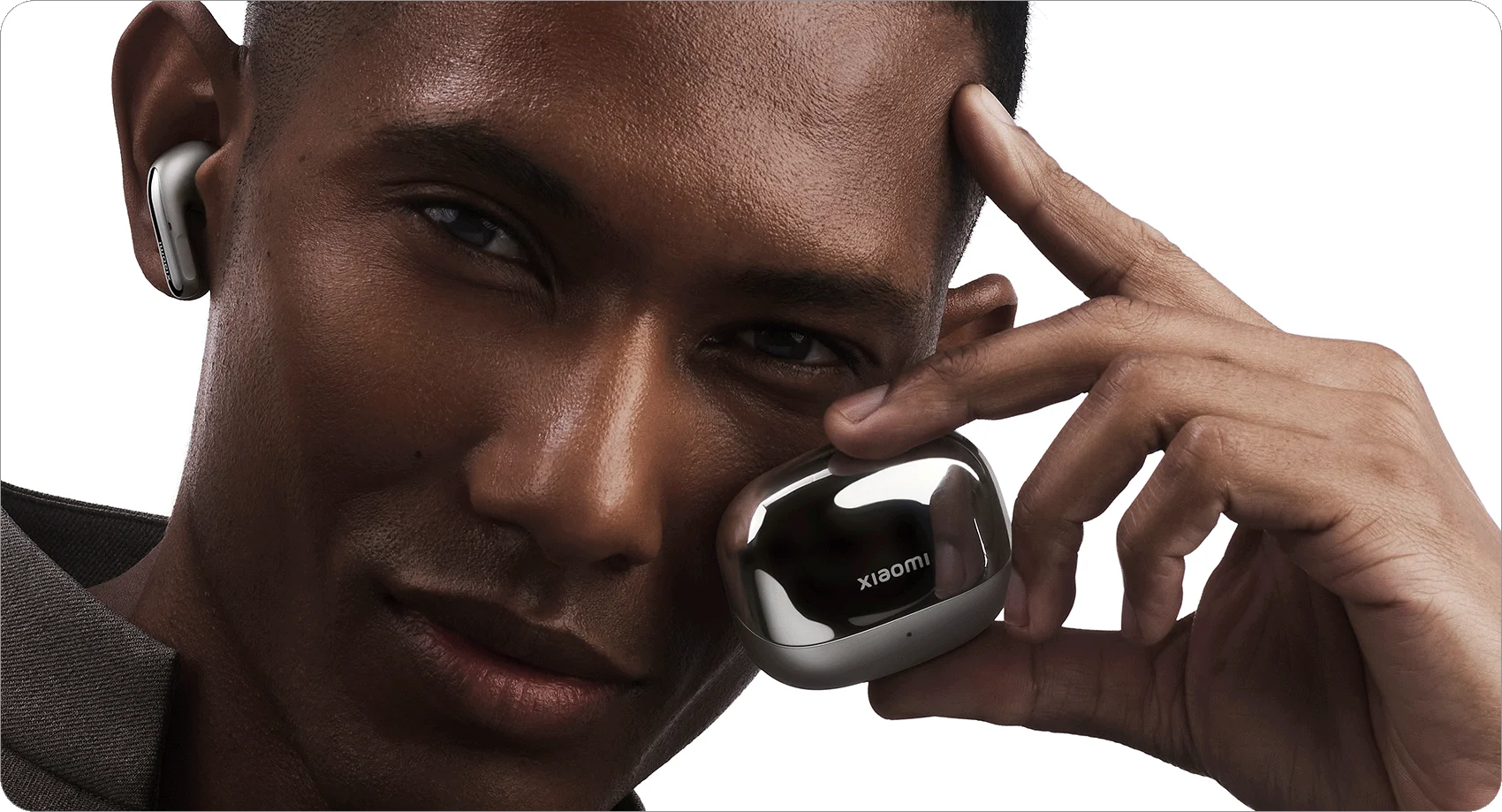 Un uomo dalla pelle scura che tiene una custodia per auricolari argentata e indossa un auricolare. Logo Xiaomi.